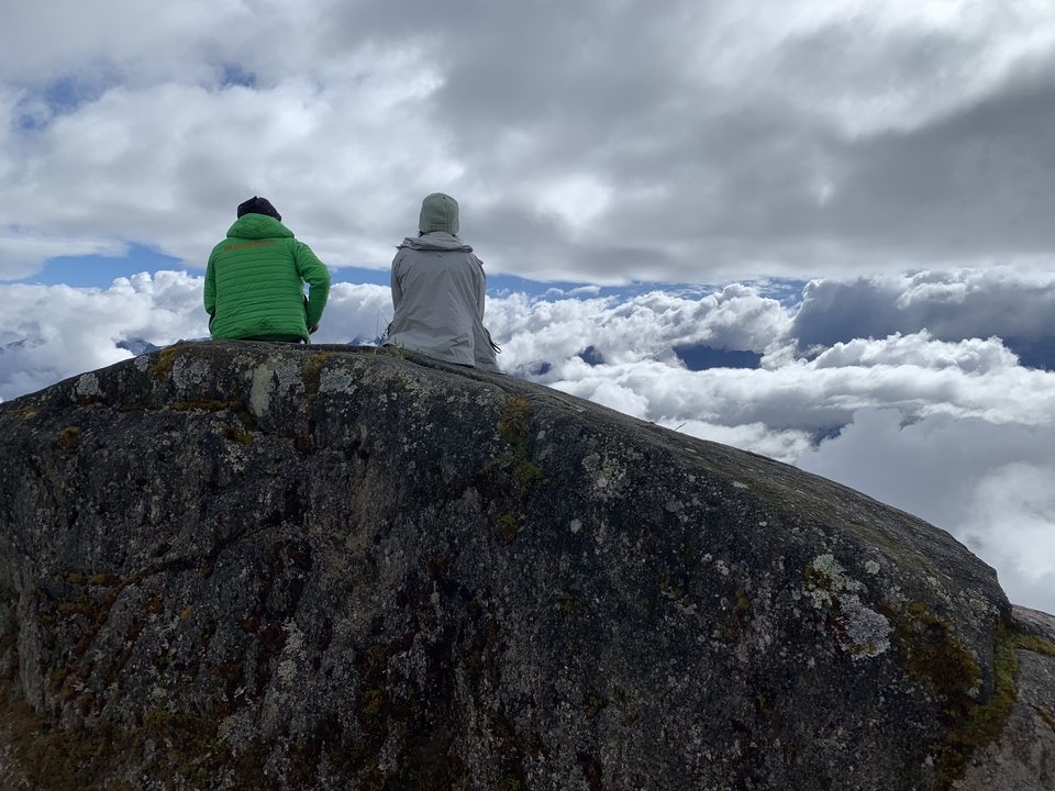 Two people sitting on a rock with clouds around.