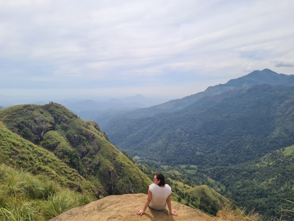Traveler gazes over lush green ridges and distant misty valleys from a high viewpoint in Ella.