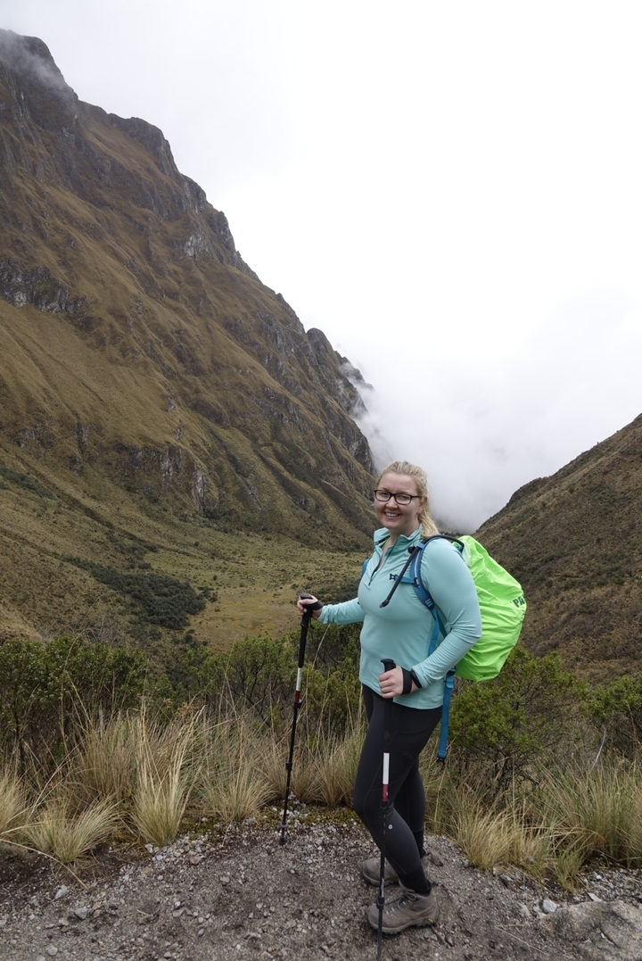 A hiker posing in a valley with misty mountains in the background.