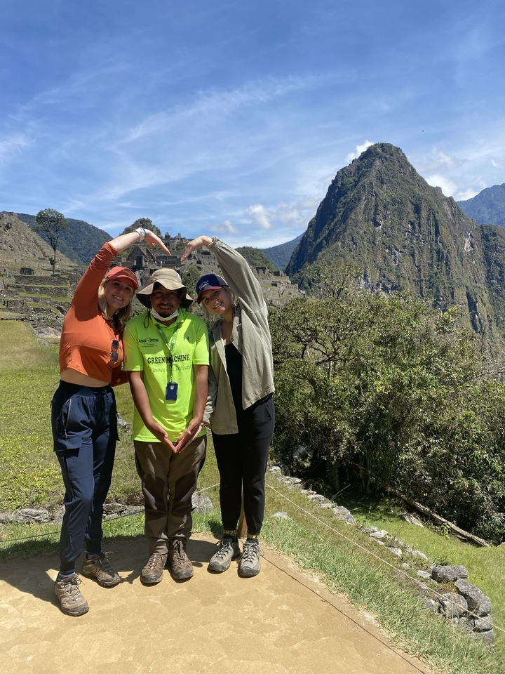 Two people and a guide at Machu Picchu forming a heart shape with arms.