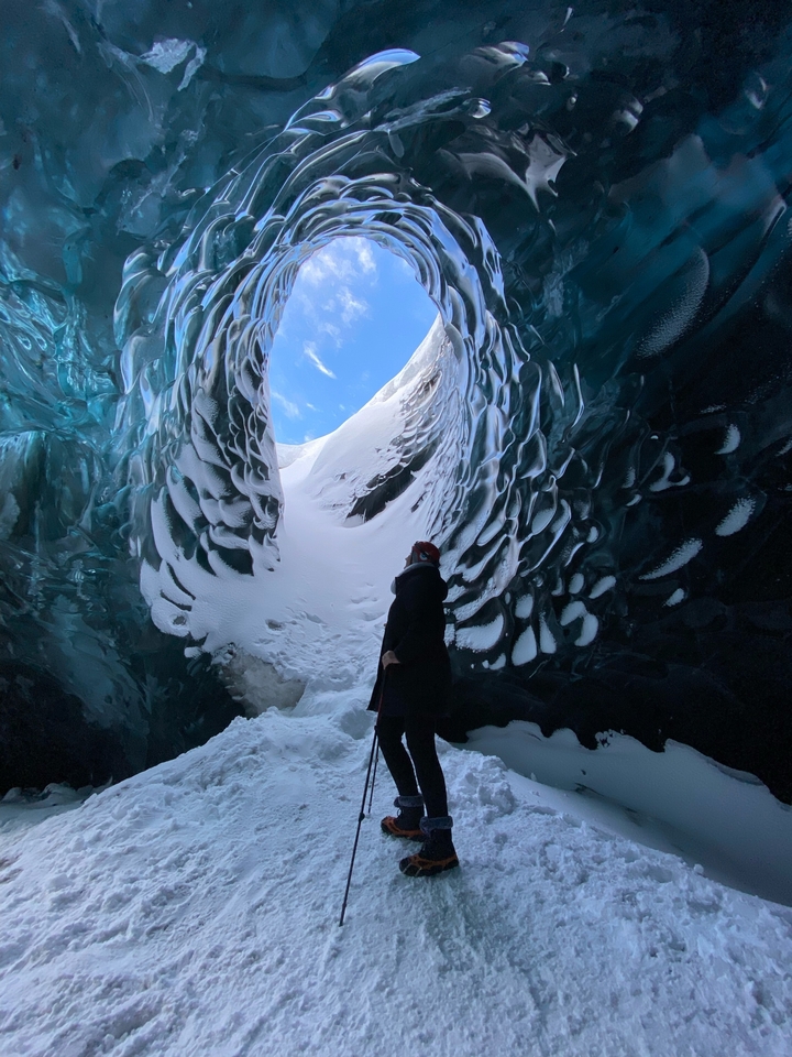 Una persona admira la vista desde el interior de la abertura de una cueva de hielo.