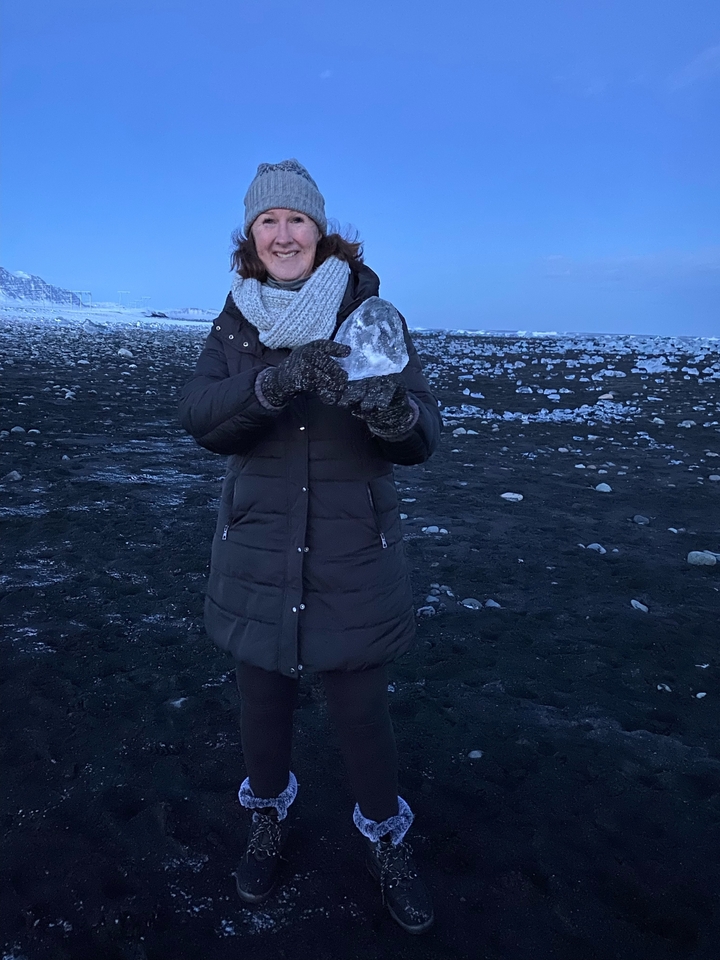 Persona sosteniendo un trozo de hielo en una playa oscura.