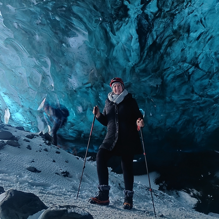 Una persona con bastones de senderismo dentro de una cueva de hielo glacial azul.