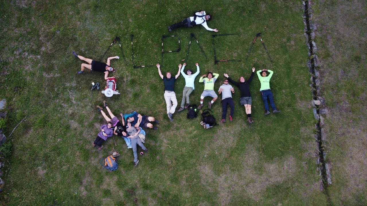 Group of people lying on grass forming the word 'ALPACA'.