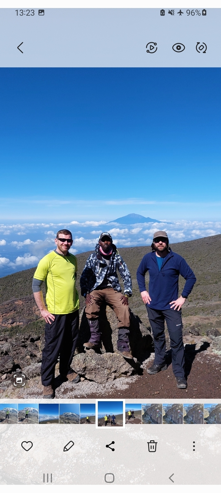 Three men posing on a mountain with distant peaks above the clouds.