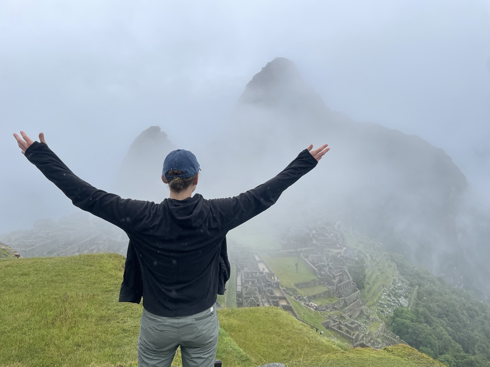 Person with arms outstretched facing Machu Picchu in mist.