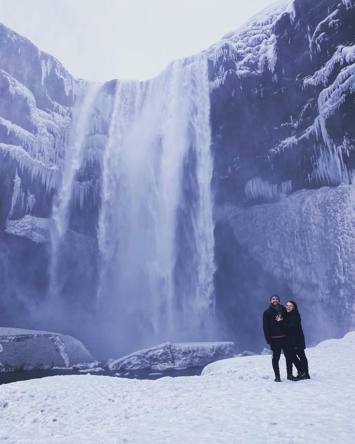 Two people standing in front of a large, partially frozen waterfall.