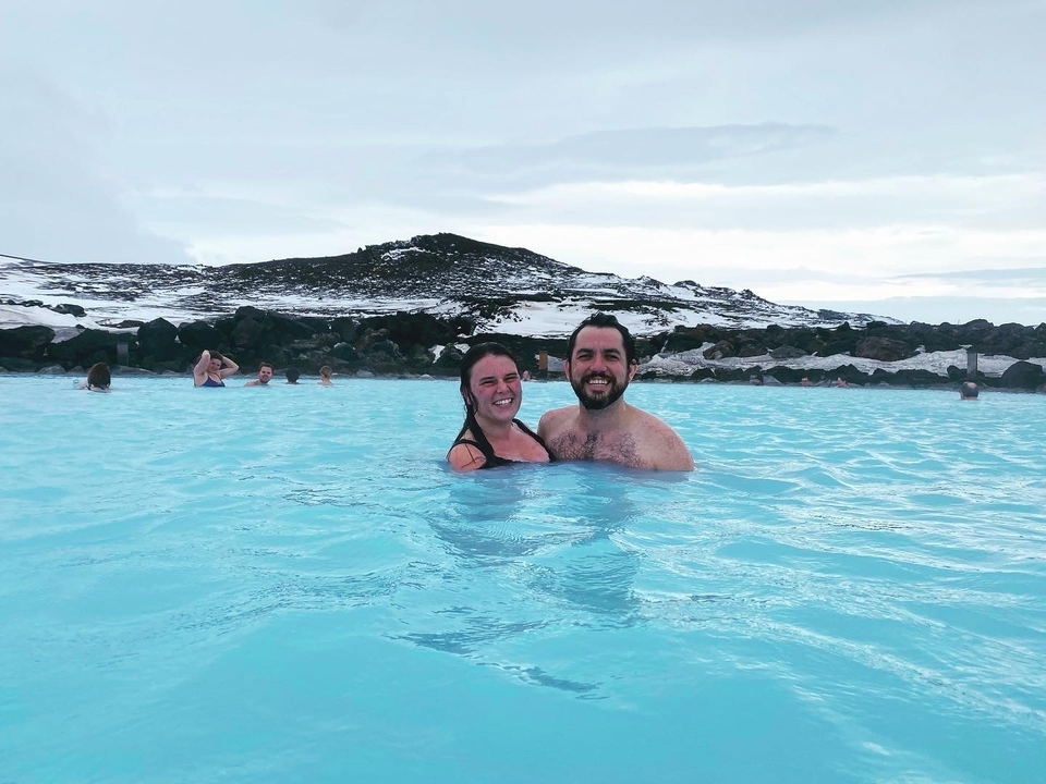 Couple enjoying a warm, natural pool with a snowy landscape in the background.