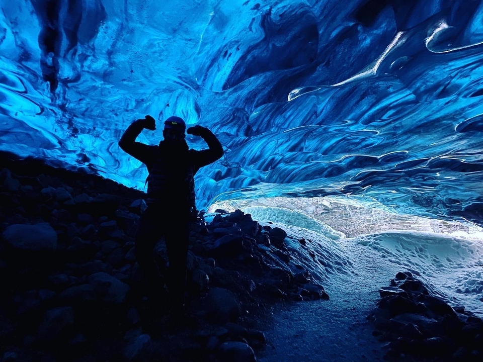 Person silhouetted in a blue ice cave with an adventurous pose.