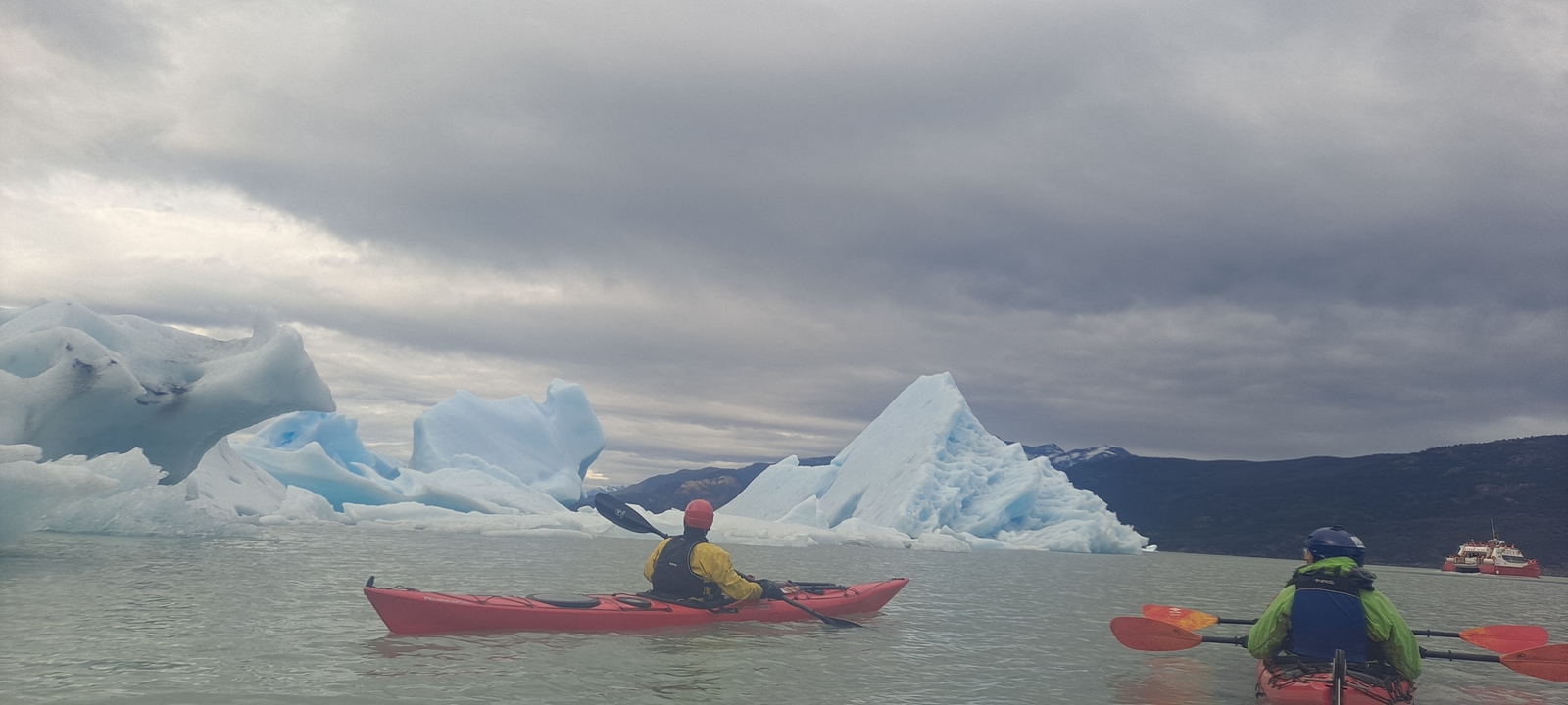 Two people kayaking near icebergs.