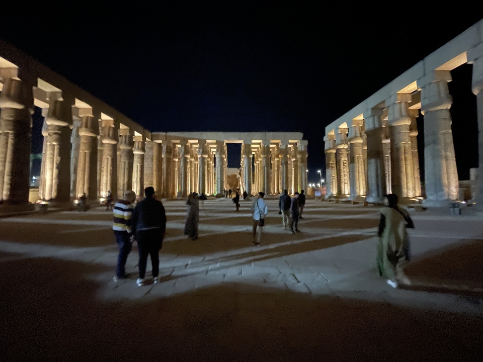 Ancient Egyptian temple lit up at night with visitors.