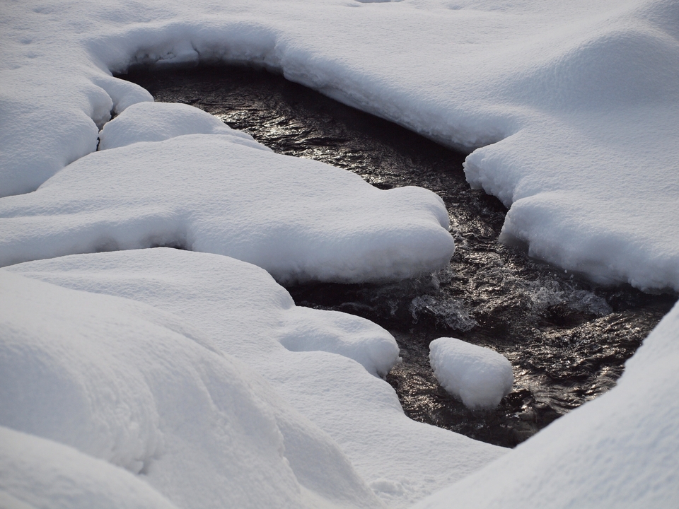 Un arroyo que fluye entre terreno cubierto de nieve.