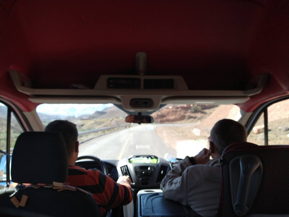 Interior view of a car with two people driving through mountainous terrain.