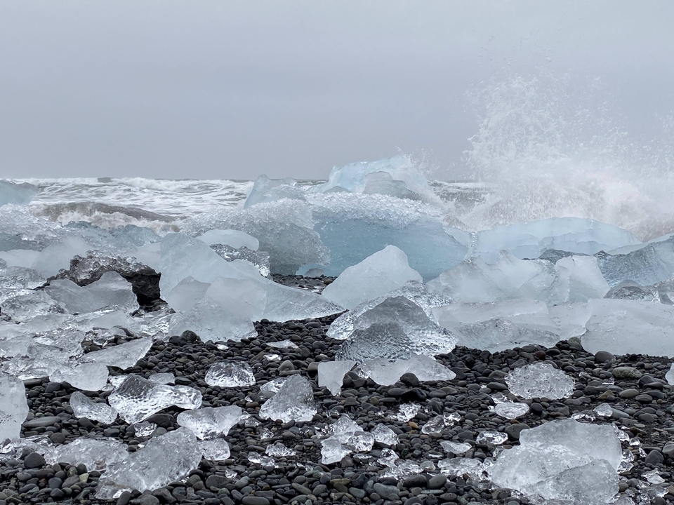 Ice formations on a black beach with waves crashing.