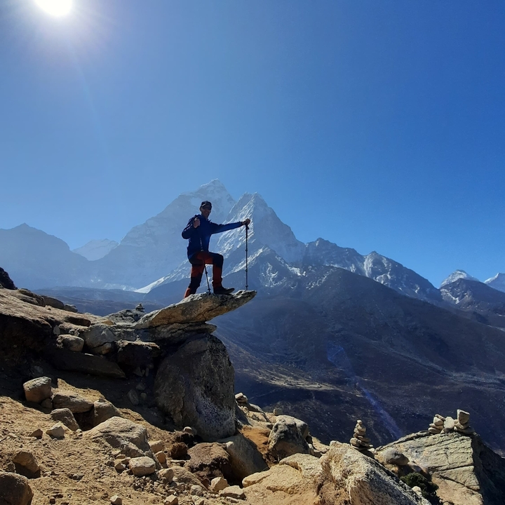 Hiker posing at the top of a peak with snowy mountains.