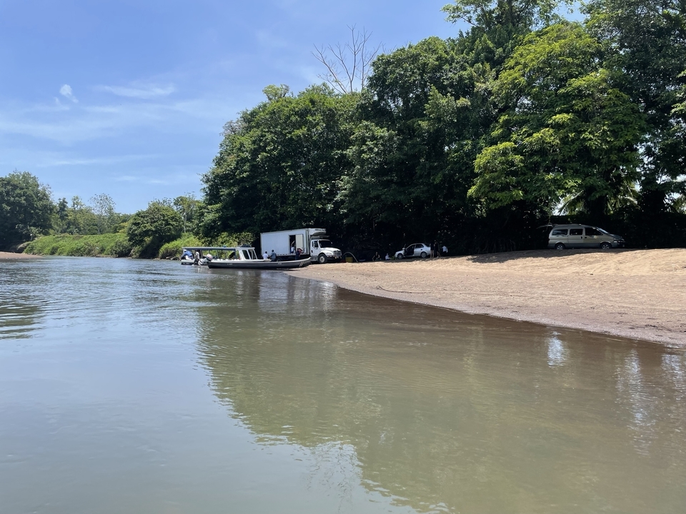 Bateau amarré sur une berge avec des véhicules et des arbres.
