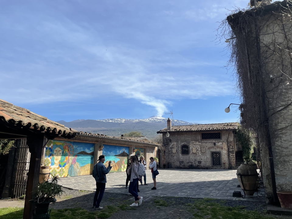 Group of people in front of a mural and distant view of Mount Etna.