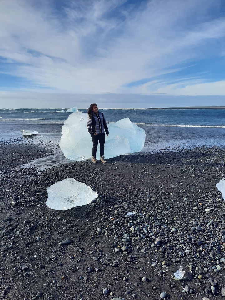 Woman standing by icebergs on a black sand beach.