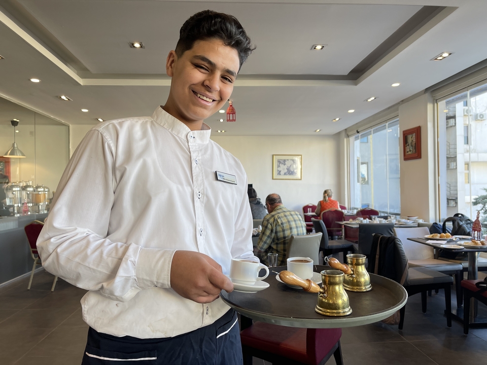 Smiling waiter holding a tray with coffee set in a restaurant.