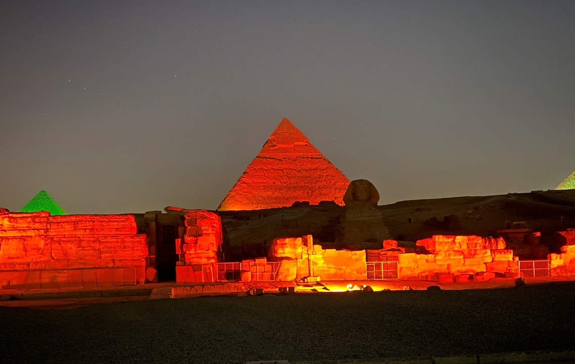 The Pyramids of Giza and the Sphinx illuminated by red and green lights at night.