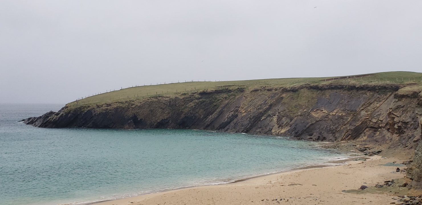 Sandy beach with a grassy cliff overlooking a bay.