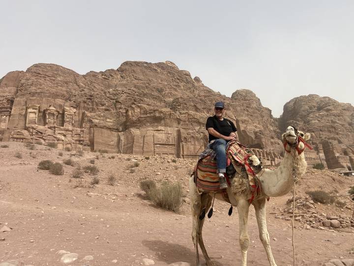 Man riding a camel in Petra desert landscape.