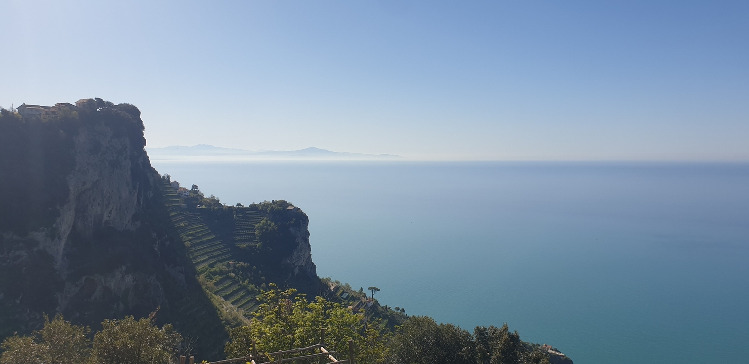 A scenic cliffside view with terraced fields and blue sea.