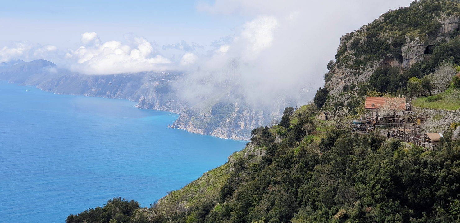 A panoramic mountain and coastal view with a house perched on the edge.