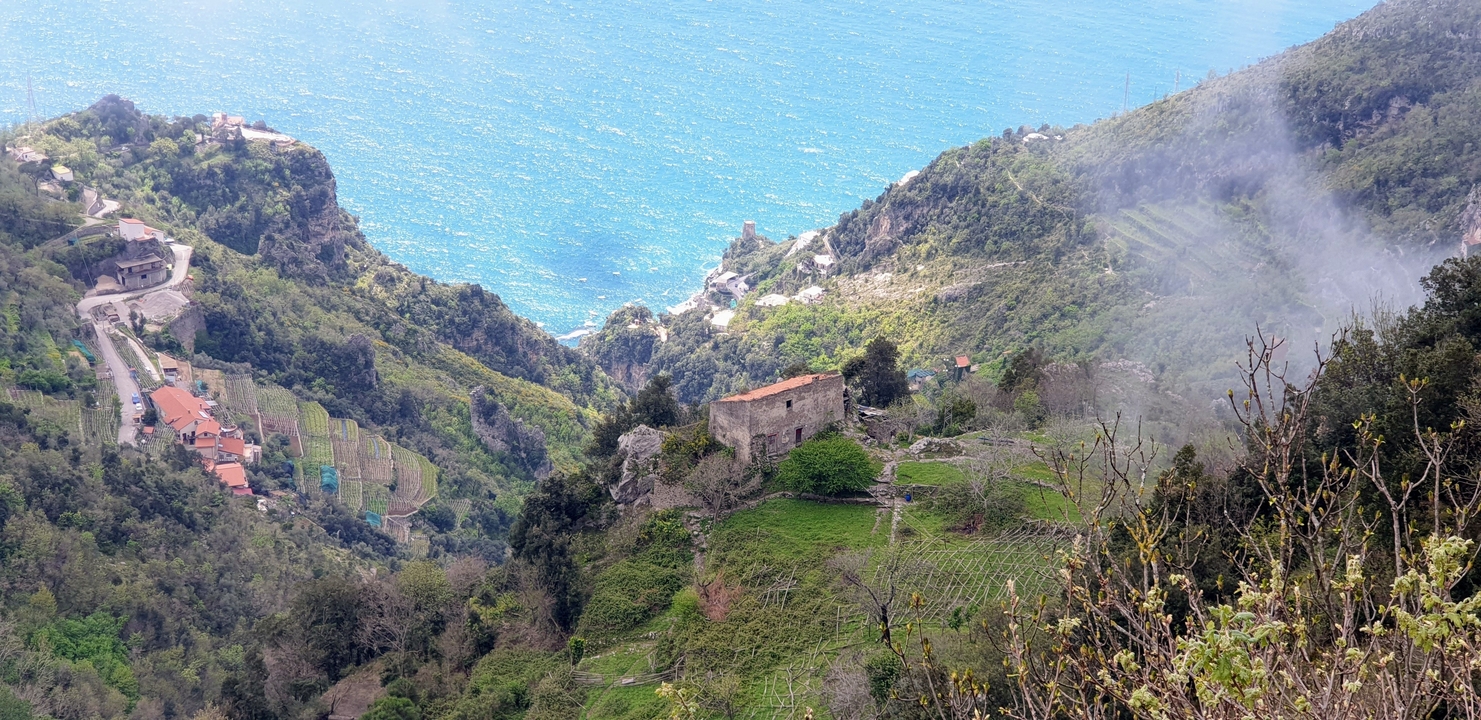 A valley view with scattered buildings and blue sea in the distance.