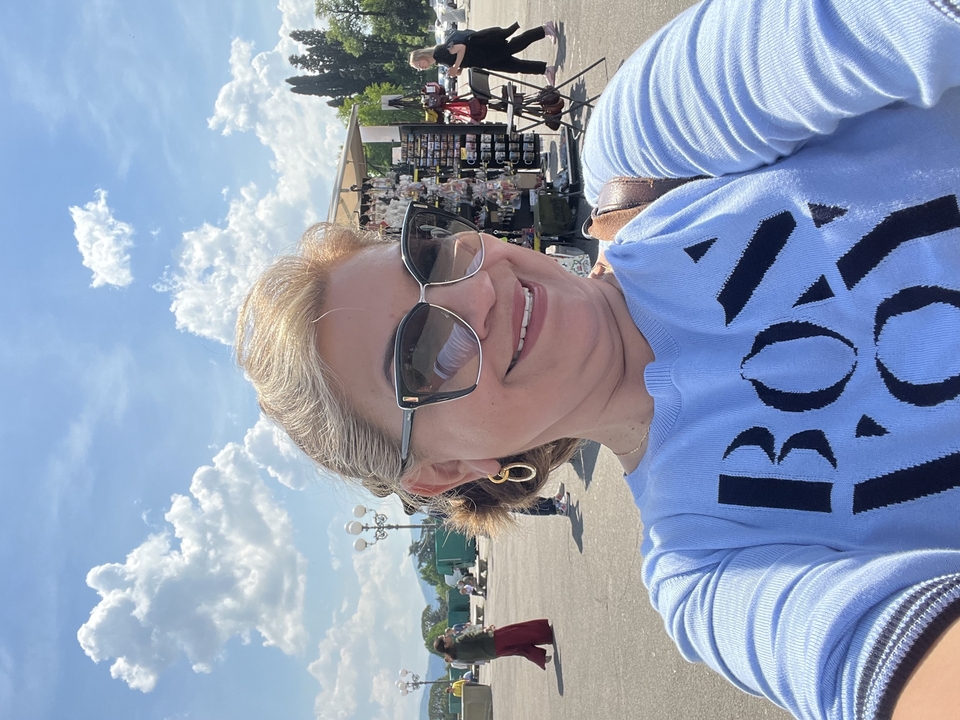 Woman smiling outdoors with a market in the background.