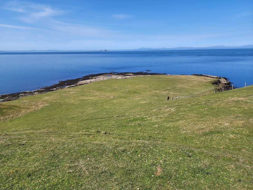 Coastal landscape with rolling grasslands and a distant view of a calm sea.