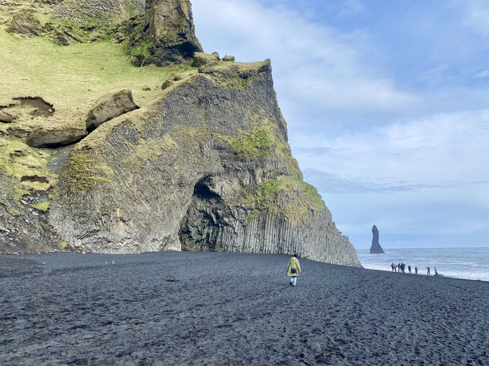 Rocky coastline with a tall sea stack and people in the distance.