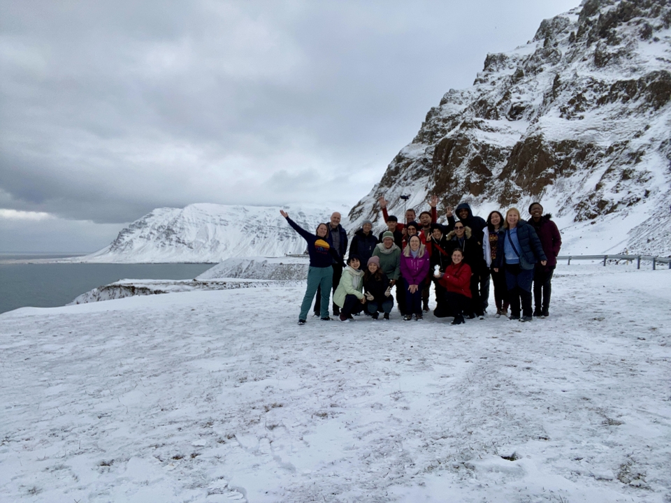Group of people posing on snowy terrain with cliffs and sea in the background.