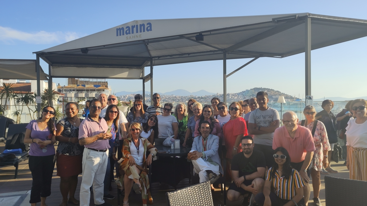 Large group of people gathered under a marina canopy by the water.
