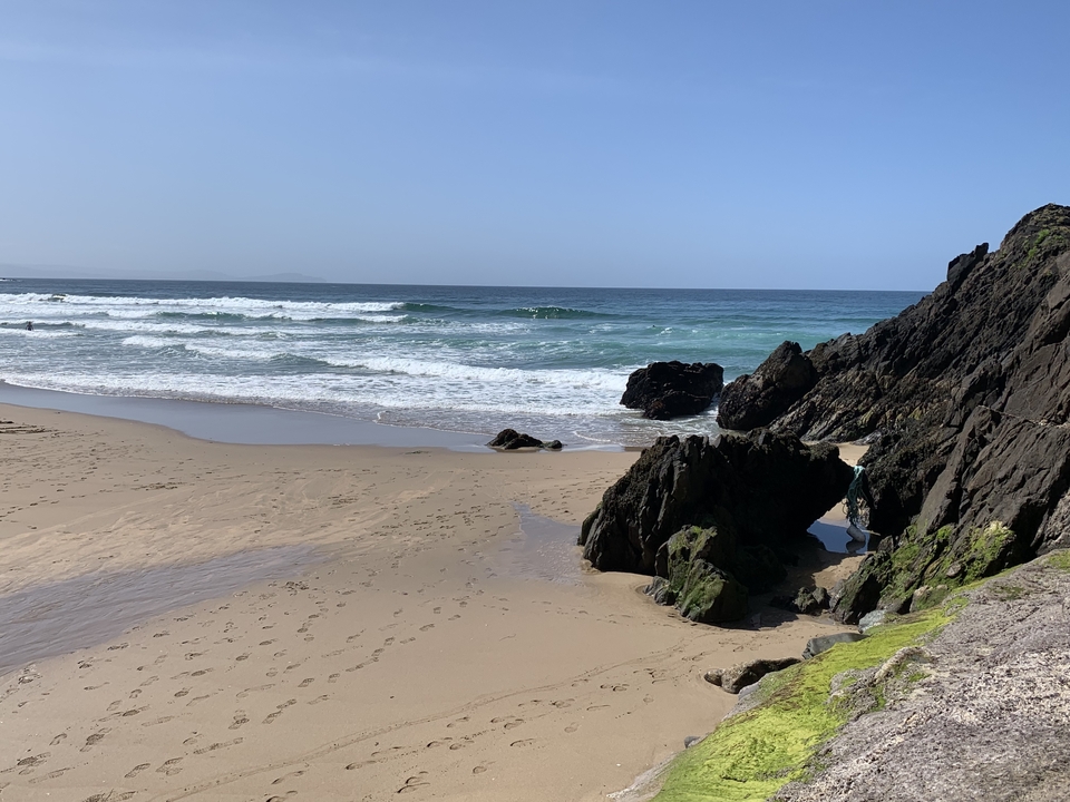 A sandy beach with ocean waves and rocks.