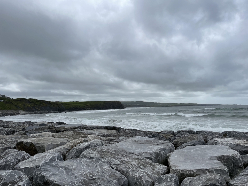 Rocky coast with waves under a cloudy sky.