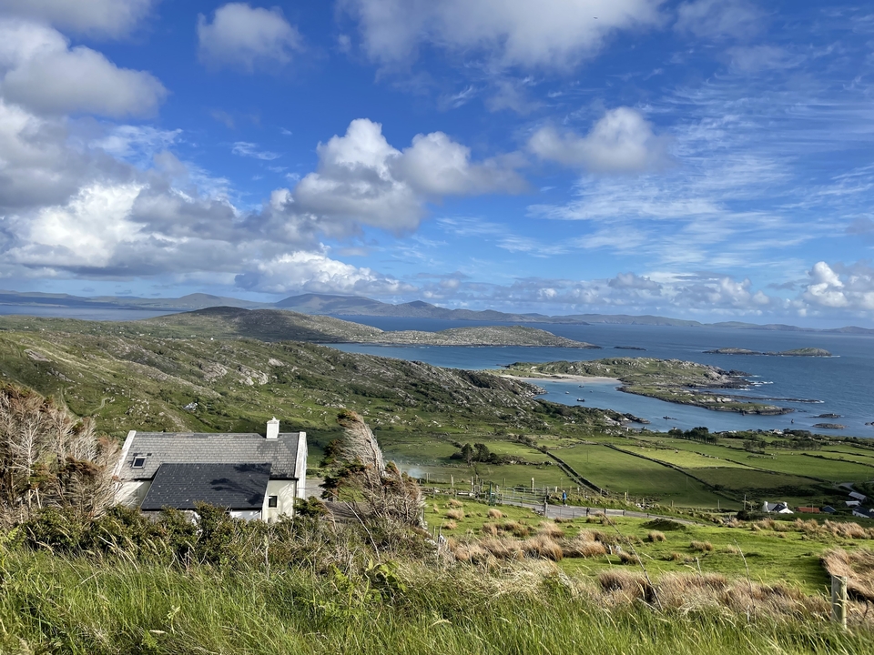 Scenic view of a coastal landscape with a house and distant mountains.