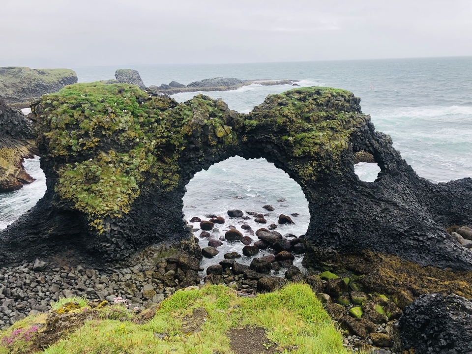 Coastal rock formation with natural arches and the ocean.