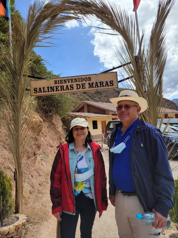 Couple standing under a welcome sign for Salineras de Maras.