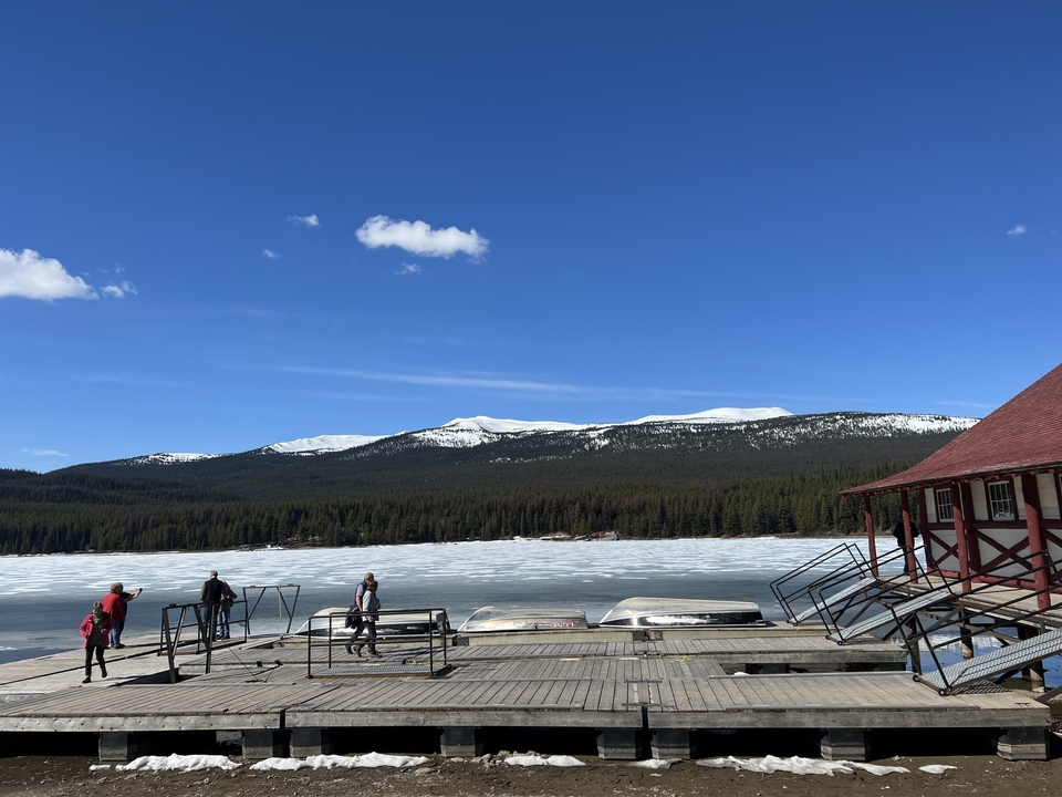 Un étang partiellement gelé avec des personnes sur un ponton montrant un paysage enneigé.