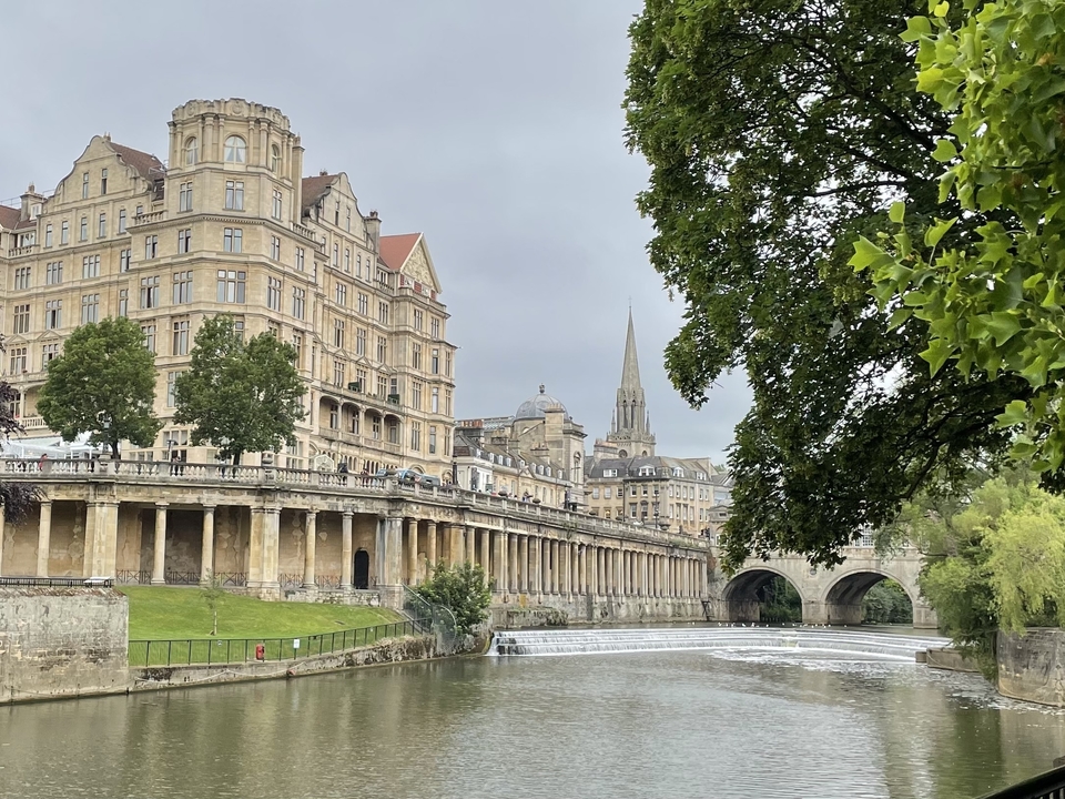 Stone buildings along a river with a bridge and trees.