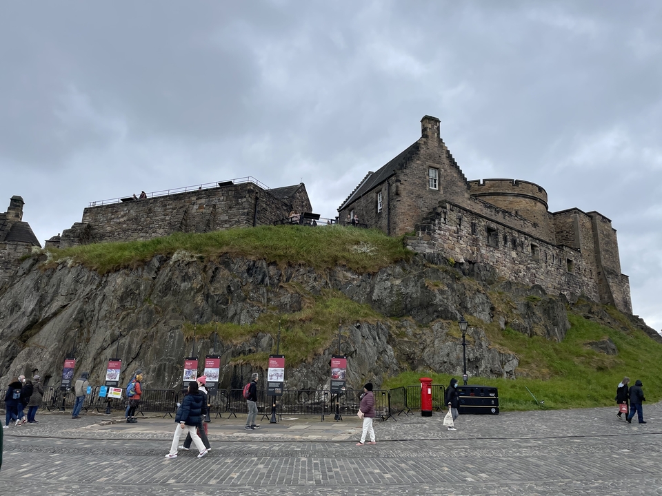 A large stone castle on a hill with people at the forefront.