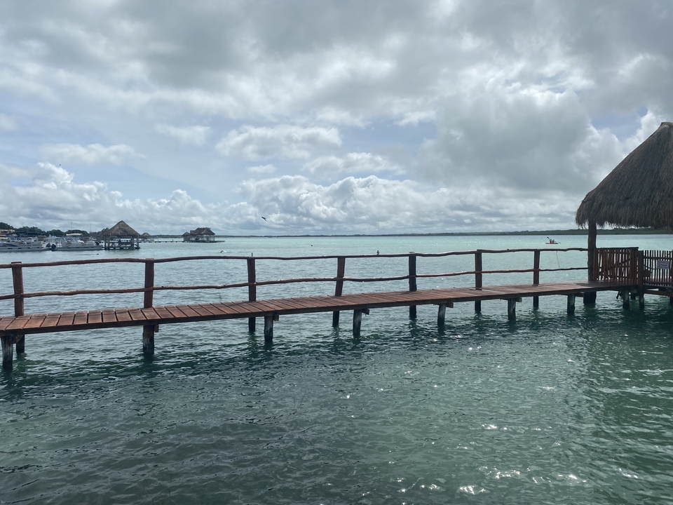 A wooden dock over a body of water with huts in the distance.