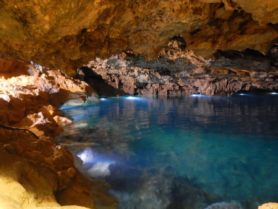 Inside of a cave with a body of water and artificial lights.