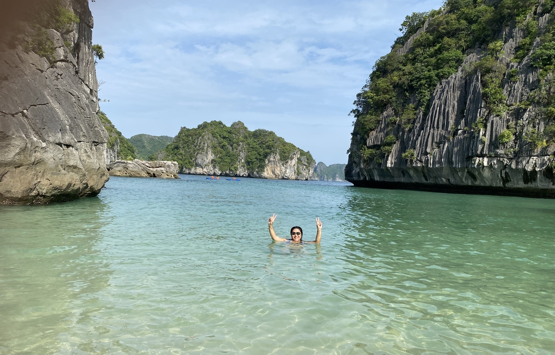 A person swimming in clear waters surrounded by limestone cliffs.