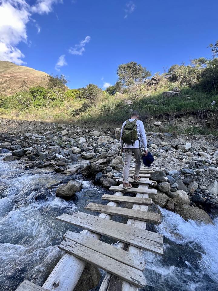 Man crossing a wooden bridge in a rocky landscape.