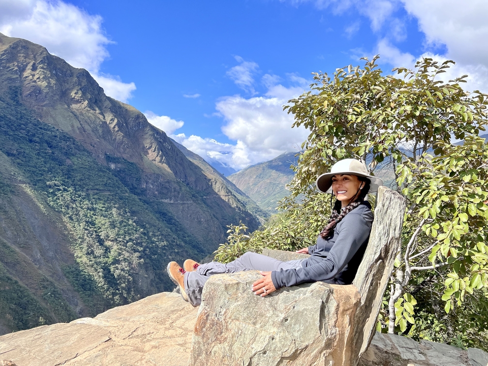 Woman enjoying the view while sitting on a large rock in a mountainous area.