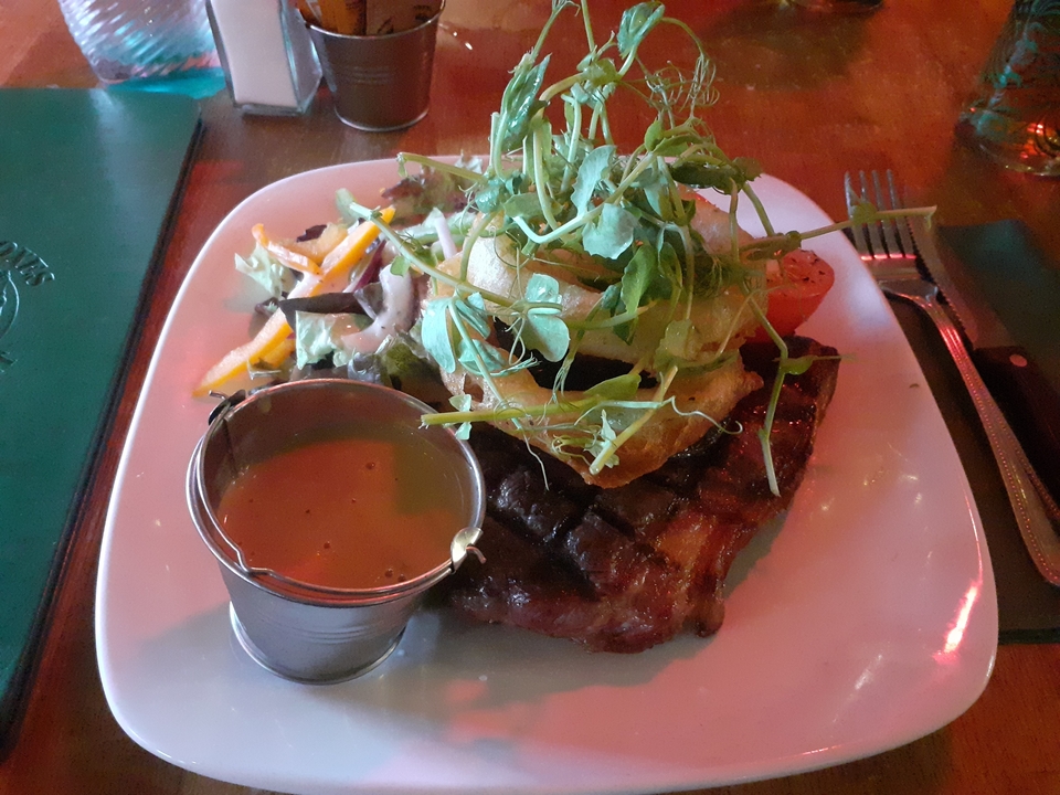 A plate of grilled steak with salad and a sauce on the side.