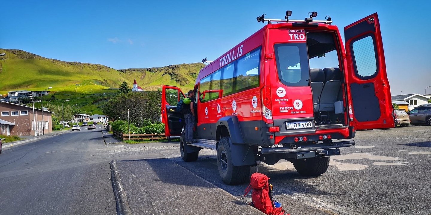 Autobus de tourisme rouge garé près d'un village et de collines