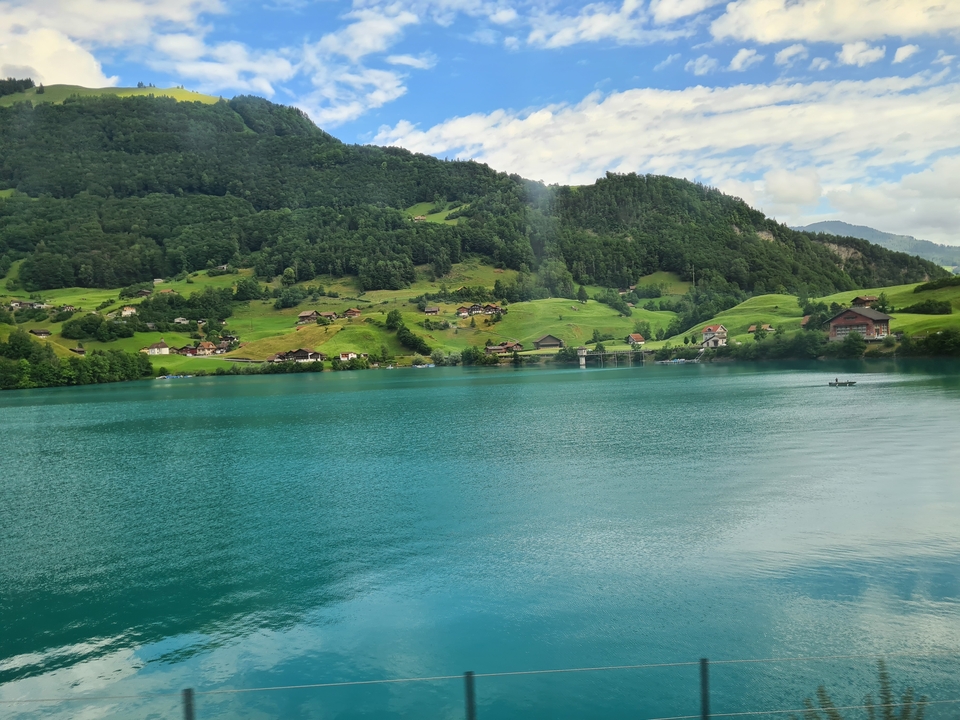 A serene lake with turquoise water surrounded by lush green hills and small houses.